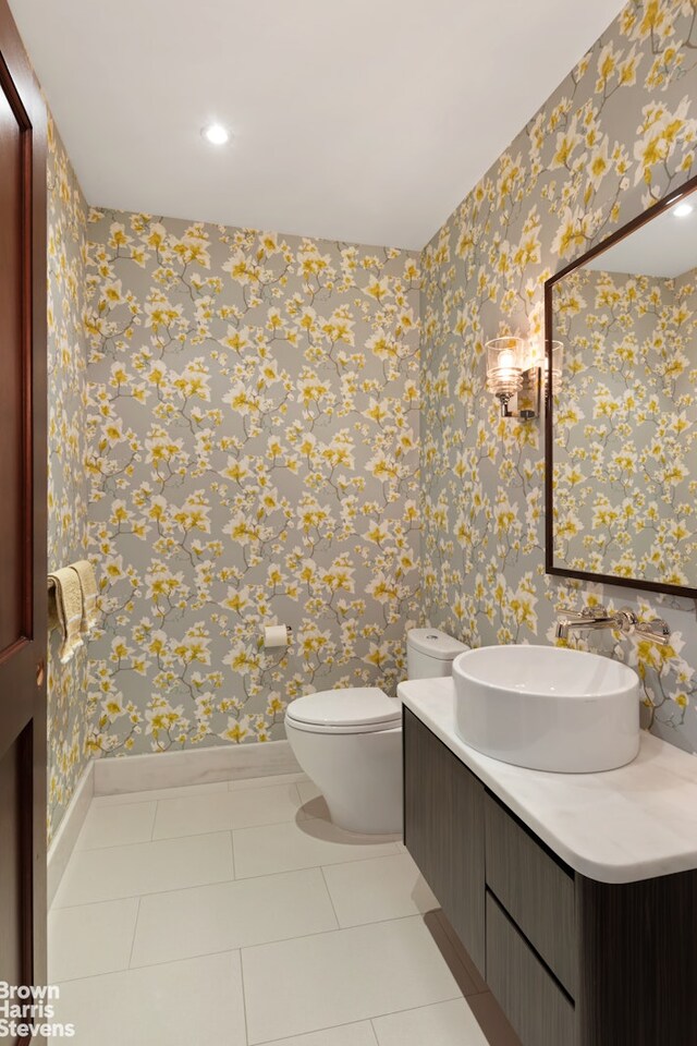 half bathroom featuring wallpapered walls, baseboards, toilet, tile patterned floors, and vanity