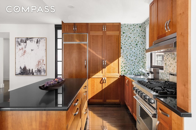 kitchen with premium appliances, dark wood-style floors, backsplash, under cabinet range hood, and a sink