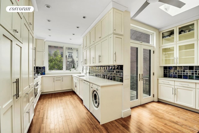 kitchen featuring backsplash, glass insert cabinets, light wood-style floors, white dishwasher, and washer / dryer