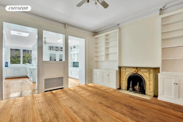 unfurnished living room featuring a skylight, ceiling fan, built in features, ornamental molding, and hardwood / wood-style flooring