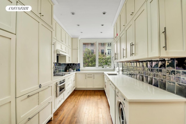 kitchen with under cabinet range hood, light wood-style floors, appliances with stainless steel finishes, decorative backsplash, and washer / dryer