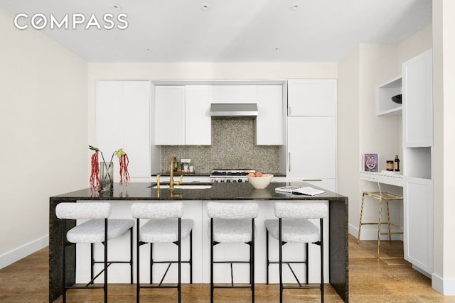 kitchen with white cabinetry, sink, a kitchen breakfast bar, decorative backsplash, and wall chimney range hood