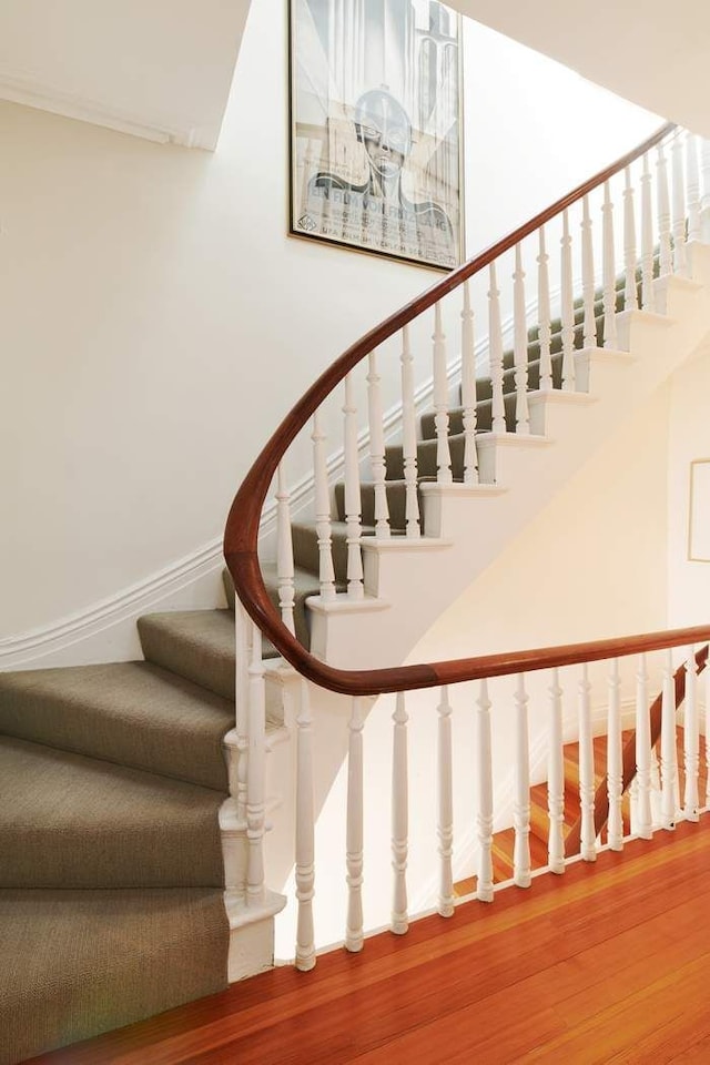 staircase featuring a towering ceiling, baseboards, and wood finished floors