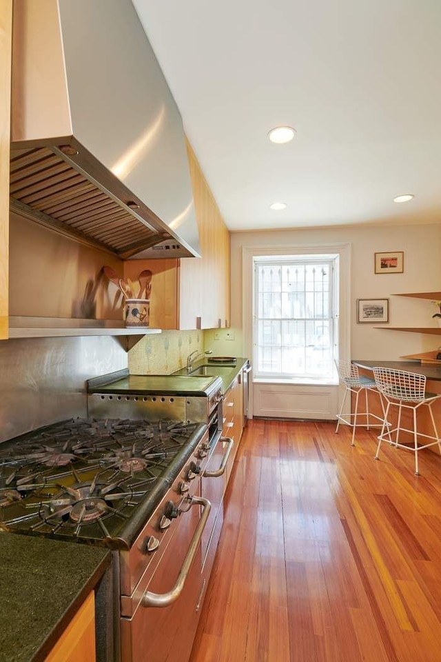 kitchen with tasteful backsplash, recessed lighting, light wood-style flooring, ventilation hood, and stainless steel gas range oven