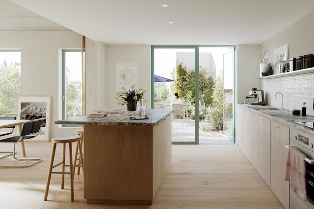 kitchen with a center island, a breakfast bar area, light wood-style flooring, a sink, and a wall of windows