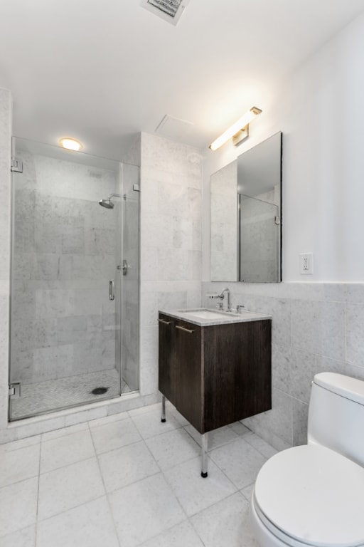 bathroom featuring toilet, vanity, tile walls, and an enclosed shower