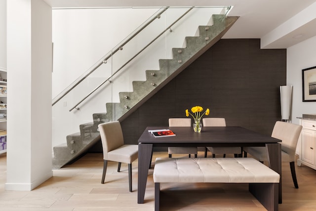 dining room with an accent wall, light wood-type flooring, baseboards, and stairs