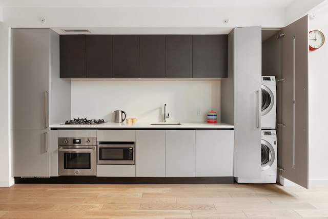 kitchen with stainless steel appliances, stacked washer / dryer, a sink, and light wood finished floors