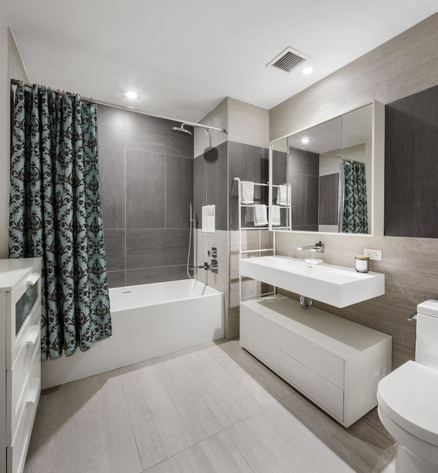 bathroom featuring toilet, a sink, visible vents, tile walls, and shower / tub combo with curtain