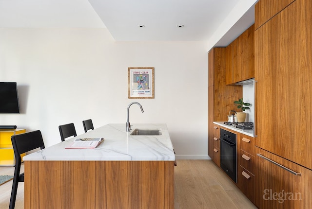 kitchen with a sink, an island with sink, modern cabinets, black oven, and a kitchen breakfast bar