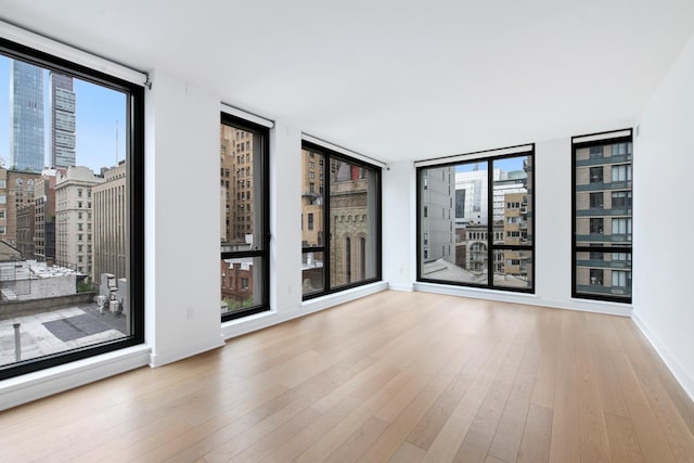 spare room with a city view, wood finished floors, baseboards, and expansive windows