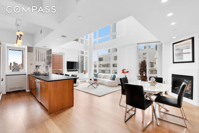 kitchen featuring light wood-type flooring, brown cabinets, dark countertops, a glass covered fireplace, and dishwasher