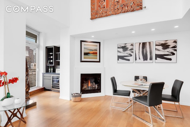 dining room featuring a glass covered fireplace, wine cooler, wood finished floors, a high ceiling, and recessed lighting