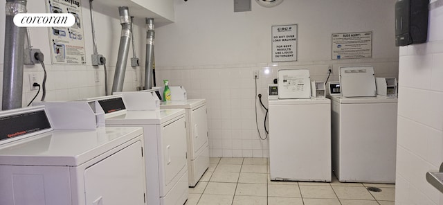 community laundry room with tile walls, washing machine and clothes dryer, light tile patterned floors, and wainscoting