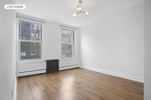 empty room featuring wood finished floors, baseboards, and baseboard heating