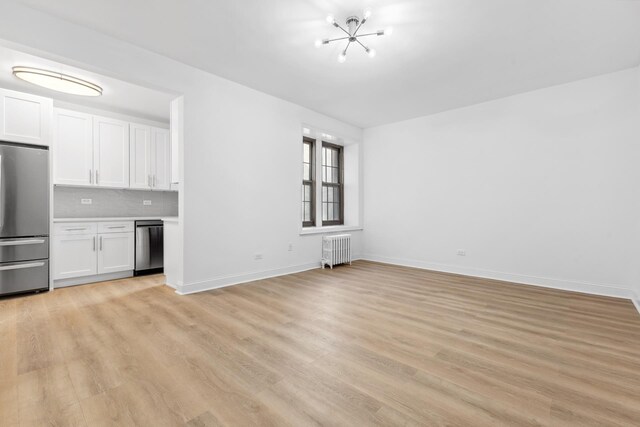 unfurnished living room with light hardwood / wood-style floors, radiator, and a notable chandelier