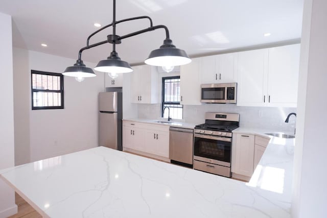 kitchen with sink, white cabinetry, pendant lighting, stainless steel appliances, and light stone countertops