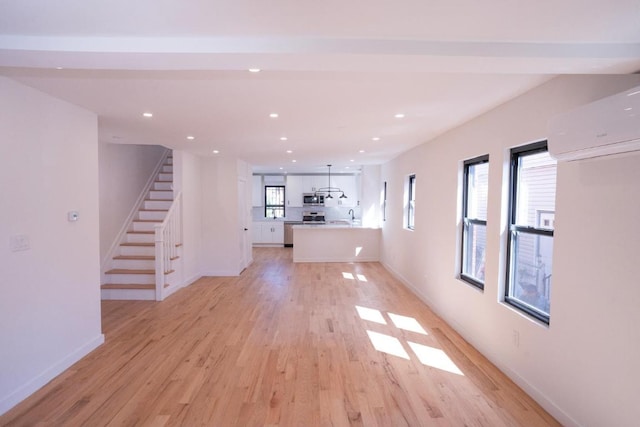 unfurnished living room featuring a healthy amount of sunlight, sink, light wood-type flooring, and an AC wall unit