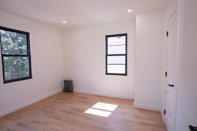 empty room featuring radiator, a wealth of natural light, and light hardwood / wood-style flooring