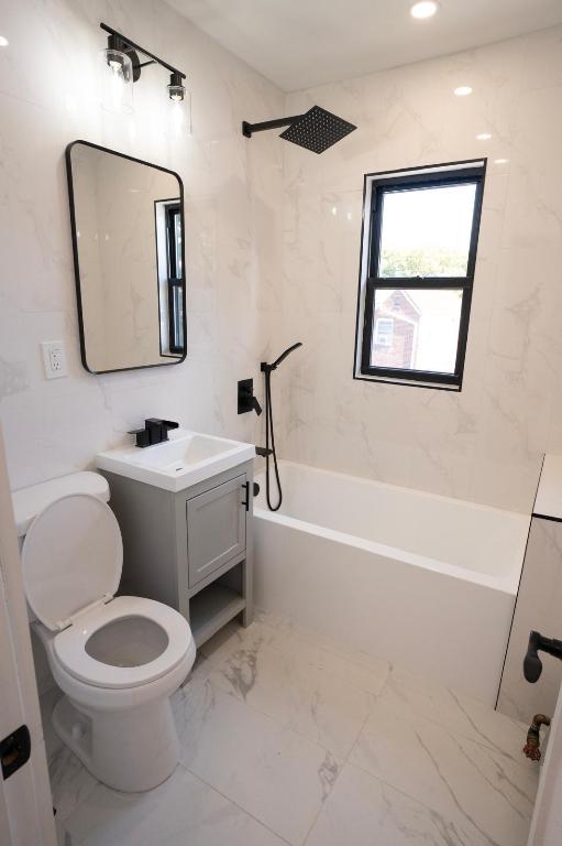 full bathroom featuring vanity, tiled shower / bath combo, tile walls, and toilet