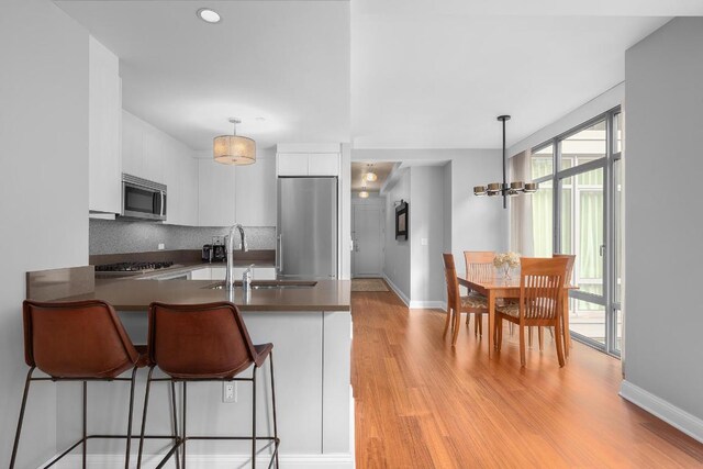 kitchen featuring kitchen peninsula, appliances with stainless steel finishes, white cabinets, and decorative light fixtures