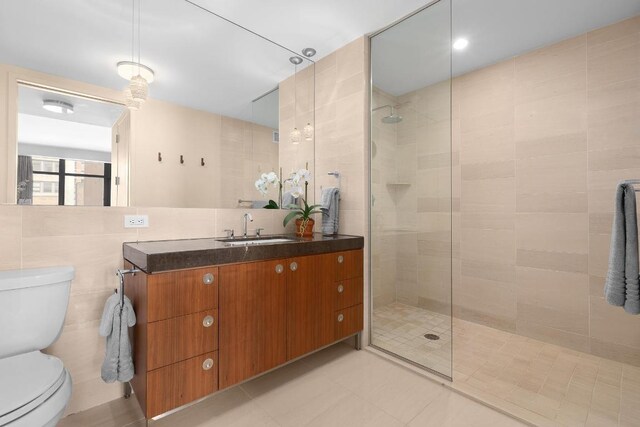 bathroom with toilet, vanity, tile walls, tile patterned floors, and a tile shower