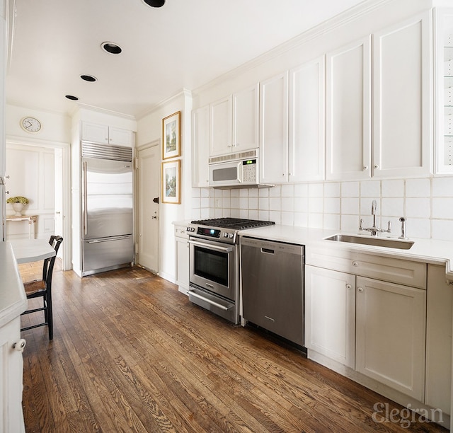 kitchen with dark wood finished floors, light countertops, decorative backsplash, appliances with stainless steel finishes, and a sink