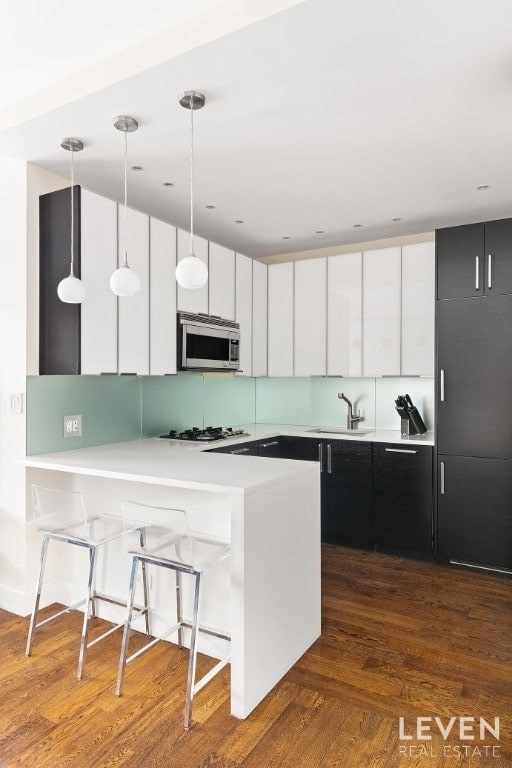 kitchen featuring pendant lighting, sink, white cabinetry, gas cooktop, and a breakfast bar area