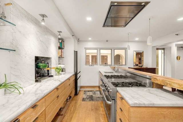 kitchen featuring stainless steel stove, decorative light fixtures, fridge, light stone counters, and light wood-type flooring