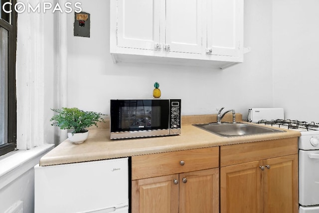 kitchen with sink, white cabinets, white range with gas stovetop, and light brown cabinets