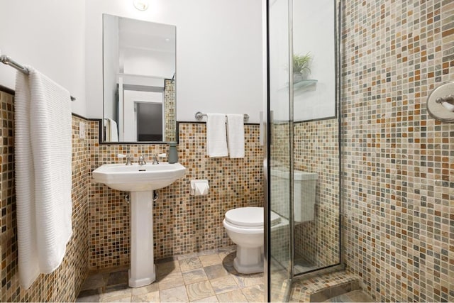 bathroom featuring toilet, sink, tile walls, and a shower with shower door