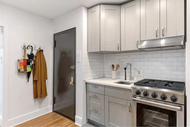 kitchen with tasteful backsplash, light hardwood / wood-style floors, sink, gray cabinets, and stainless steel range with gas stovetop