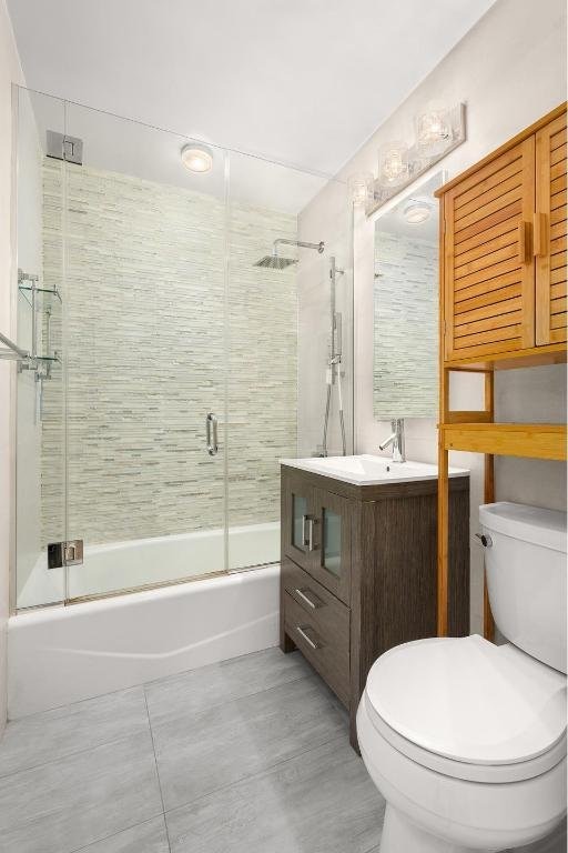 full bathroom featuring vanity, bath / shower combo with glass door, and toilet