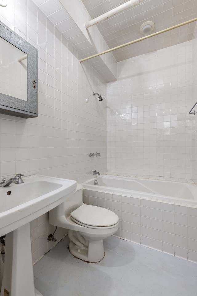 bathroom with toilet, a sink, backsplash, tiled shower / bath combo, and tile walls