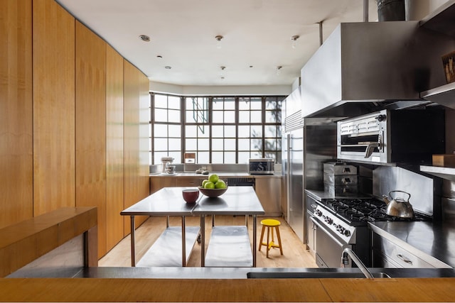 kitchen with ventilation hood, light wood-type flooring, stainless steel counters, brown cabinets, and appliances with stainless steel finishes