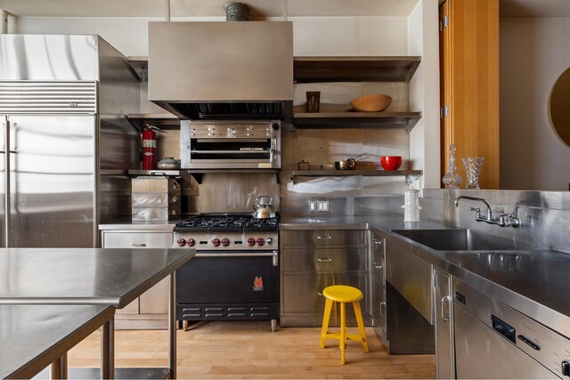 kitchen with stainless steel countertops, premium appliances, a sink, and open shelves