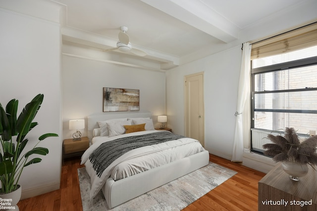 bedroom featuring light wood finished floors, beamed ceiling, and a ceiling fan