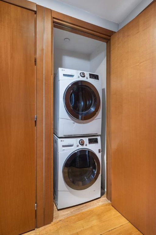 washroom featuring stacked washing maching and dryer and light hardwood / wood-style flooring