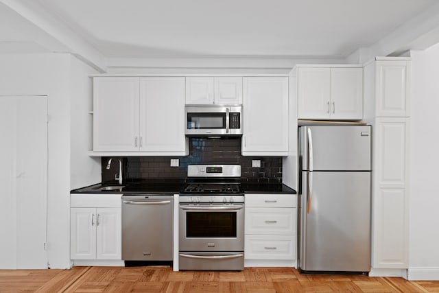 kitchen with stainless steel appliances, white cabinetry, light parquet floors, and backsplash