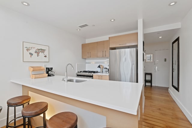 kitchen featuring sink, a breakfast bar area, stainless steel refrigerator, kitchen peninsula, and light hardwood / wood-style floors