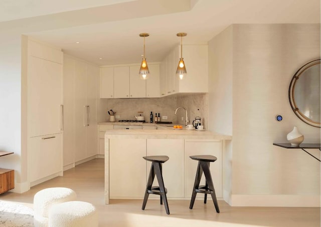 kitchen with hanging light fixtures, a breakfast bar area, white cabinets, decorative backsplash, and kitchen peninsula