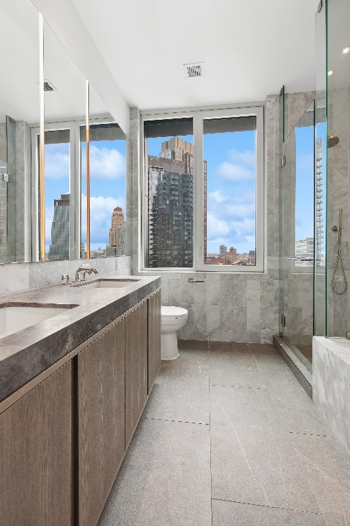 bathroom with vanity, toilet, a shower with shower door, and tile walls