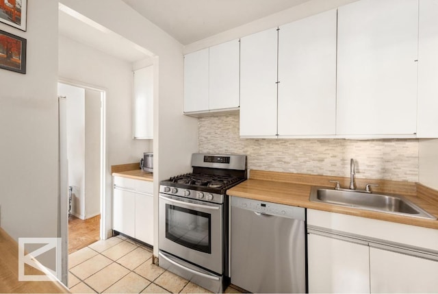 kitchen with sink, light tile patterned floors, white cabinetry, stainless steel appliances, and decorative backsplash