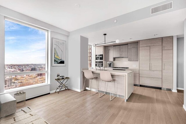 kitchen with hanging light fixtures, a kitchen island, a breakfast bar area, and light hardwood / wood-style floors