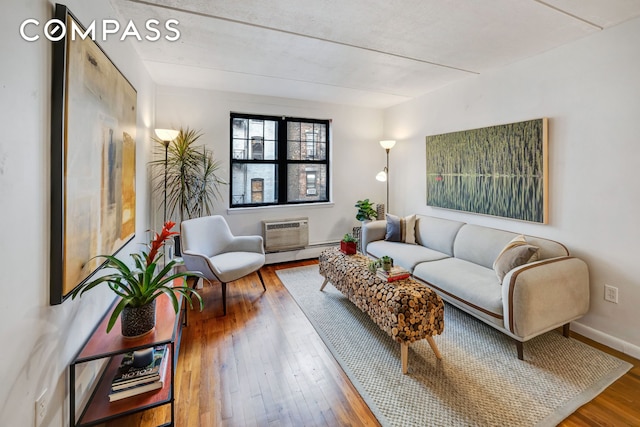 living area with a baseboard heating unit, hardwood / wood-style floors, a wall mounted air conditioner, and baseboards