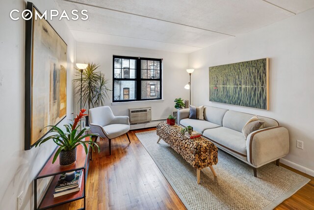 living room featuring wood-type flooring, baseboard heating, and a wall unit AC