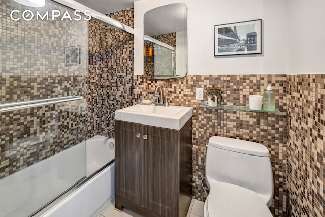 full bathroom with tile walls, toilet, vanity, wainscoting, and shower / bath combination with glass door