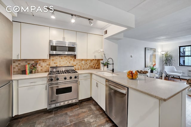 kitchen featuring a peninsula, open floor plan, backsplash, stainless steel appliances, and a sink