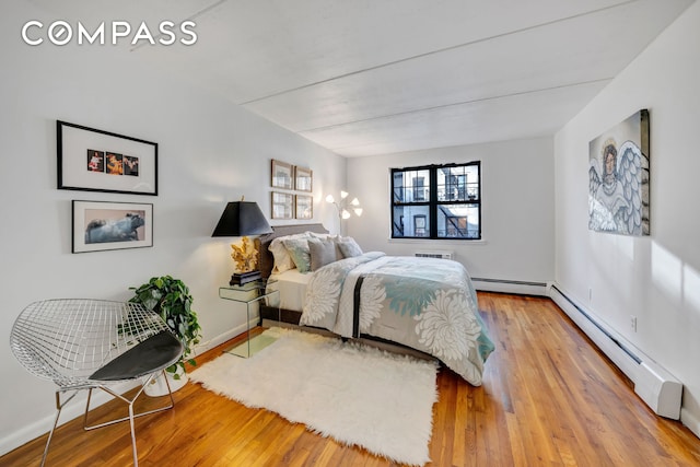 bedroom with wood finished floors, a baseboard heating unit, and baseboards