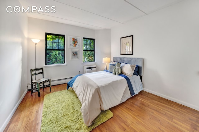 bedroom featuring a baseboard radiator, an AC wall unit, baseboards, and wood finished floors